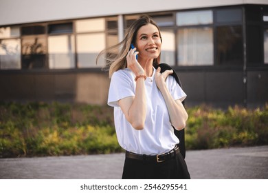 Beauty short hair woman holding jacket over shoulder. Professional businesswoman happily answering a phone call near office. Happy caucasian female using a mobile phone to communicate with partners. - Powered by Shutterstock