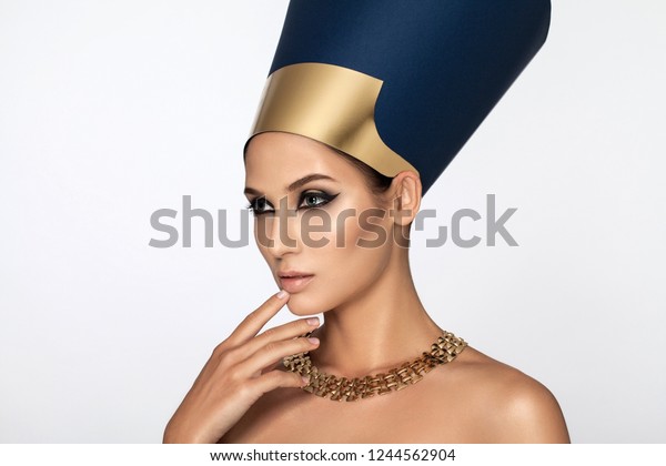 Beauty shot in Egyptian style. Beautiful adult girl in Nefertiti. Luxury and wealth. Golden decoration. Makeup, rough look. White background.