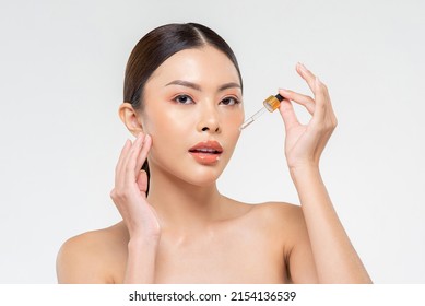 Beauty Shot Portrait Of Attractive Asian Woman Applying Skincare Product On Face From Pipette In White Isolated Background