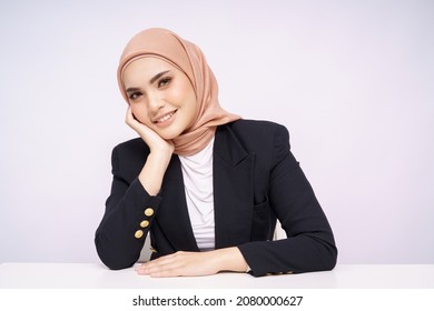 A beauty shot of a pretty young Asian hijab corporate girl with smooth glowing skin smiling and relaxing on a table over white background studio. Beauty skin care, office concept.