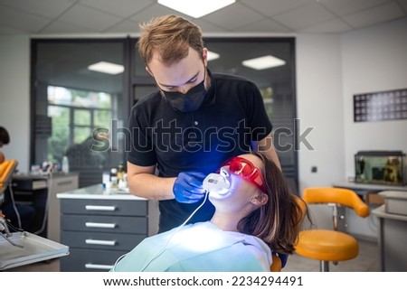 beauty is sitting in a special chair where the dentist and the assistant will perform dental treatment under a UV lamp. Concept of beautiful teeth through treatment.dentistry