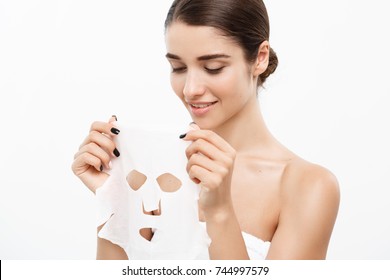 Beauty Skin Care Concept - Beautiful Caucasian Woman Applying Paper Sheet Mask On Her Face White Background.