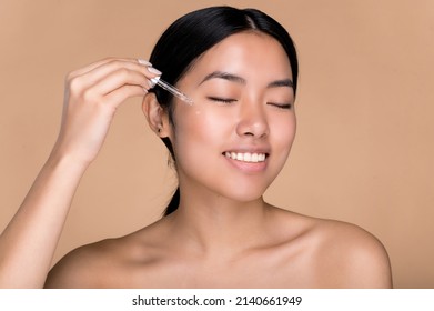 Beauty, Skin Care Concept. Pretty Chinese Young Beauty Woman With Perfect Skin And Nude Shoulders, Care Face Skin, Apply Face Oil, Moisturizing Hyaluronic Serum, Eyes Closed, Isolated Beige Background