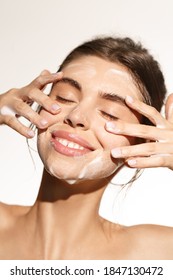Beauty and skin care concept. Topless woman smiling while cleaning her face with nourishing cleansing foam with hyaluronic acid, close eyes, rubbing cheeks for deep hydration, white background. - Shutterstock ID 1847130472