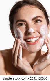 Beauty and skin care concept. Topless woman smiling while cleaning her face with nourishing cleansing foam with hyaluronic acid, rubbing cheeks, watching facial skin, white background - Shutterstock ID 2051460860
