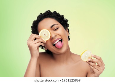 Beauty, Skin Care And Detox Concept - Beautiful African American Woman Making Eye Mask Of Lemons Over Lime Green Natural Background