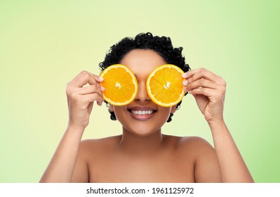 Beauty, Skin Care And Detox Concept - Smiling Beautiful African American Woman Making Eye Mask Of Oranges Over Lime Green Natural Background