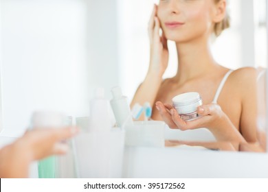 beauty, skin care and people concept - close up of smiling young woman applying cream to face mirror reflection at home bathroom - Powered by Shutterstock