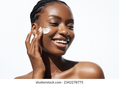 Beauty and skin care. Skincare hydration and oil balance. Portrait of African American woman with afro braids hairstyle is applying a cream smear on her face and standing against white background - Shutterstock ID 2342278775
