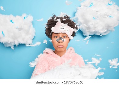 Beauty Skin Care Treatment Bedtime Concept. Sad Frustrated African American Woman Holds Pillow Applies Nose Patch To Get Rid Off Black Dots Dressed In Nightwear Upset After Awakening Feathers Around