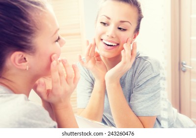 Beauty skin care. Young beautiful teenage girl touching her face before the mirror, enjoying her clean skin. Pretty woman touching her cheek and smiling. Perfect pure skin. Fresh Clean Skin. Skincare 