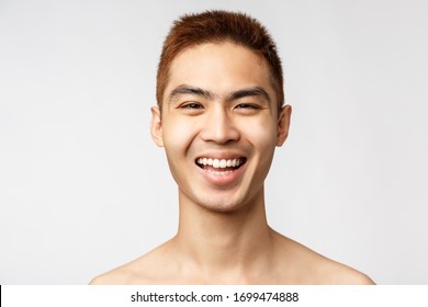 Beauty, skincare and men health concept. Headshot of enthusiastic handsome asian man with naked torso, laughing and smiling joyfully, advertisement of cosmetics products, white background