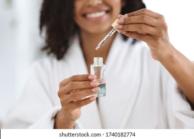 Beauty And Skincare. Smiling Black Woman Holding And Opening Bottle With Moisturizing Face Serum, Making Skin Treatment At Home, Closeup