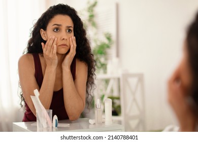 Beauty and skincare. Upset young woman looking in mirror and touching face, examining wrinkles and dark circles under her eyes at home, copy space. Dull tired skin concept - Shutterstock ID 2140788401