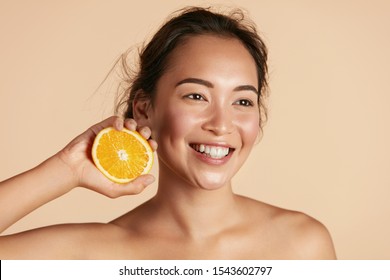 Beauty. Smiling Woman With Radiant Face Skin And Orange Portrait. Beautiful Smiling Asian Girl Model With Natural Makeup, Healthy Smile And Glowing Hydrated Facial Skin. Vitamin C Cosmetics Concept