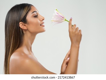 Beauty Spa Face Model Profile over White. Young Woman with tanned Skin Smelling Lily Flower. Beautiful Brunette Girl with Long Straight Hair happy smiling Side View over Gray