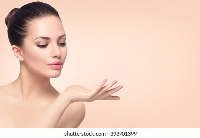 Beauty Spa Woman with perfect skin Portrait. Beautiful Brunette Spa Girl showing empty copy space on the open hand palm for text. Proposing a product. Gestures for advertisement. Beige background