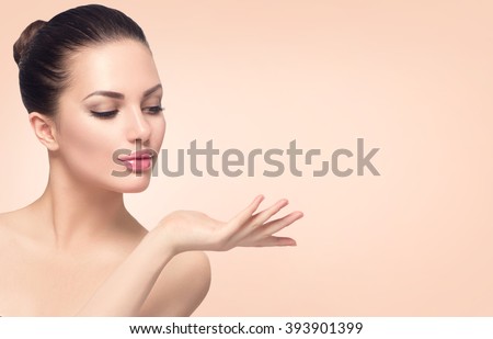 Beauty Spa Woman with perfect skin Portrait. Beautiful Brunette Spa Girl showing empty copy space on the open hand palm for text. Proposing a product. Gestures for advertisement. Beige background