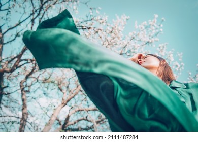 Beauty spring fashion model girl posing over blooming trees, enjoying nature in spring apple orchard. Beautiful brunette young woman over sky in Garden with blooming trees. blossom flowers outdoors