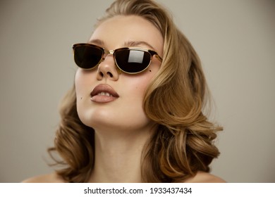 Beauty studio portrait of young happy optimistic cheery beautiful blonde  woman with perfect skin, make up and hairstyles, posing with sunglasses naked isolated over grey wall background