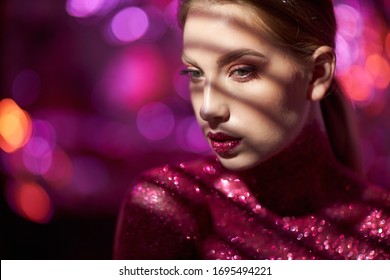 Beauty, style and fashion concept.Beautiful young Caucasian woman with sparkles on her face, chest and neck, has professional makeup isolated on a pink background. Creative art on the face.