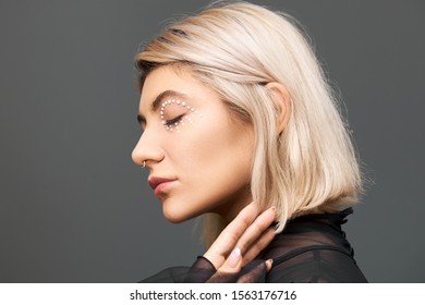 Beauty, Style, Fashion, Glamour And Femininity Concept. Fashionable Stylish Young Female With Dyed Bob Hairstyle, Nose Ring And White Crystals Around Her Eye, Posing Isolated With Eyes Closed