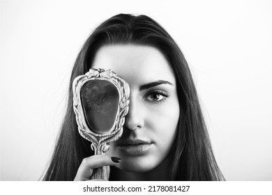 Beauty, style and make-up concept. Black and white portrait of beautiful woman covers her one eye with old vintage dirty mirror. Model with natural make-up, long dark hair and looking to camera