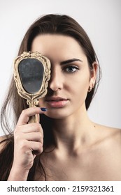 Beauty, style and make-up concept. Portrait of beautiful woman covers her one eye with old vintage dirty mirror. Model with natural make-up, long brown hairs and looking to camera with blue eye