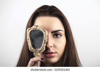 Beauty, style and make-up concept. Portrait of beautiful woman covers her one eye with old vintage dirty mirror. Model with natural make-up, long brown hairs and looking to camera with blue eye