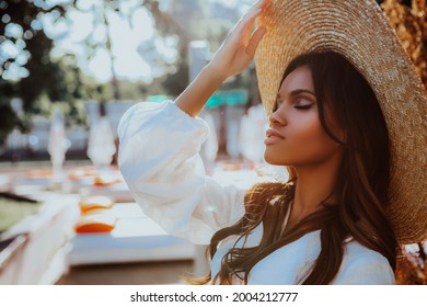 Beauty styled portrait of a young African - American woman in the sun at sunset. Fashion black girl posing in a straw hat while relaxing by the pool.            
