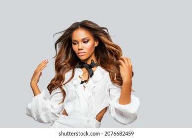 Beauty Styled Portrait Of A Young African - American Woman In White Dress. Makeup. Fashion African - American Girl With Curly Hair Posing In The Studio On A Light Background. Isolated. Studio Shot.  