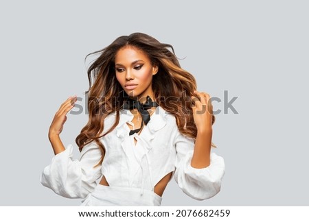 Beauty styled Portrait of a young African - American Woman in White Dress. Makeup. Fashion African - American Girl with Curly Hair posing in the Studio on a light background. Isolated. Studio shot.   