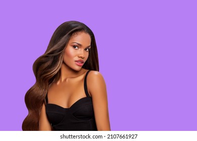 Beauty Styled Portrait Of A Young African-American Woman With Long Curly Hair In Black Dress. Makeup. Fashion Black Woman With Curly Hair Posing In The Studio On A Light Purple   Background. Isolated.