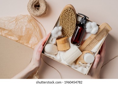 Beauty subscription Box preparation. Female hands holding gift box with natural skincare products, body brush, shampoo, soap, moisturizer.