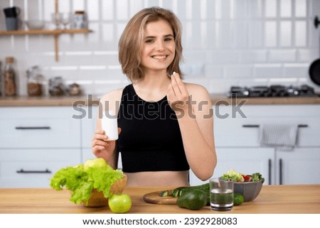 Beauty supplement. Attractive young woman holding vitamin capsule and glass of  water  at the kitchen. Healthy lifestyle, healthy diet nutrition concept