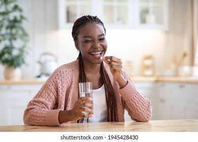 Beauty Supplements. Positive Young Black Female Taking Vitamin Pill And Drinking Water At Home, Smiling African Lady Using Multivitamin Tablet For Beautiful Skin, Hair And Nails, Looking At Camera