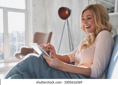 Beauty surfing the net. Attractive young woman using digital tablet and smiling while sitting on the sofa at home - Shutterstock ID 1005616369