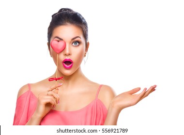 Beauty Surprised Young Fashion Model Girl With Valentine Heart Shaped Cookie In Hand. Love. Beautiful Young Woman Pointing Hand, Advertising Gesture. Valentines Day Gift. Isolated On White Background.