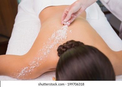 Beauty therapist pouring salt scrub on womans back in the health spa