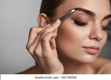 Beauty Tools. Closeup Of Woman Beautiful Face With Professional Perfect Makeup Closed Eyes And Tweezers. Sexy Girl Plucking Brows Hair. Metal Forceps For Eyebrows. High Resolution Image