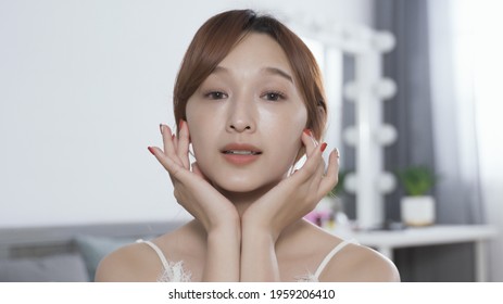 beauty vlogger demonstrating the right way of to applying skin product on face. pretty lady facing camera using both hands to lightly massage moisturizer into face, smiling after action is done.