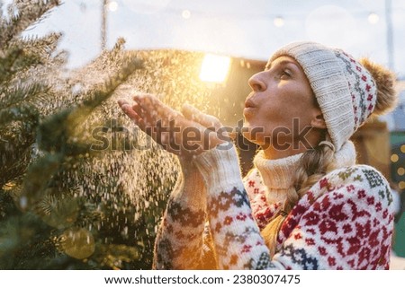 Beauty Winter Girl Blowing Snow on her selected Christmas tree at a Christmas Tree market.