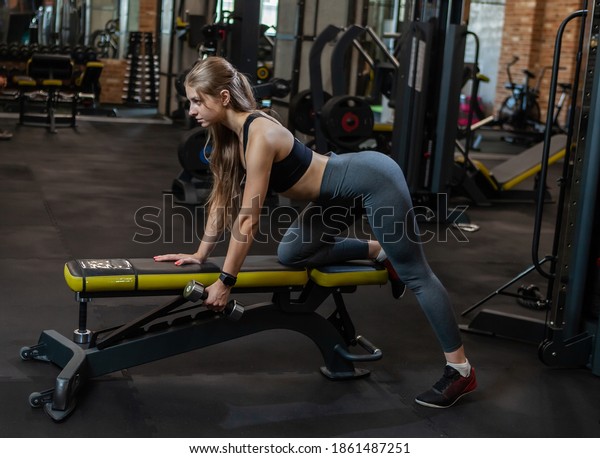Beauty Woman bodybuilder in gym lifting dumbbells on\
bench at modern gym