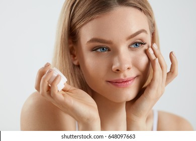 Beauty Woman Face. Closeup Of Beautiful Young Female Model With Fresh Skin Holding Cream Bottle In Hand. Portrait Of Sexy Girl Applying Cosmetic Product Under Eyes. Skincare Concept. High Resolution