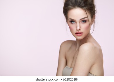 Beauty Woman Face. Closeup Of Beautiful Young Female Model With Fresh Natural Skin And Professional Facial Makeup On Pink Background. Portrait Of Sexy Girl With Glamour Hair Style. High Resolution