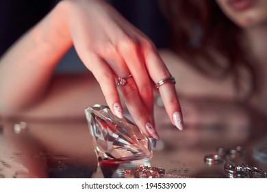 Beauty Woman holds big diamond in hand while lying on table. Beautiful hands, professional manicure, large diamond brilliant