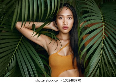 Beauty. Woman model with long straight hair and palm leaves. Asian girl with beautiful exotic face at tropical nature