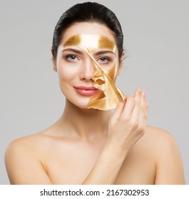 Beauty Woman Peeling Off Golden Facial Mask. Smooth Skin Model Taking Off Gold Purifying Face Film Mask Over Gray. Women Cleansing Cosmetics And Skincare Cosmetology