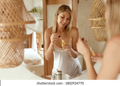 Beauty. Woman In Silk Pajama Applying Essential Oil On Face. Lady In Elegant Home Clothing Using Skincare Product With Hyaluronic Acid Or Serum Collagen For Anti-Aging And Anti-Wrinkle Treatment.