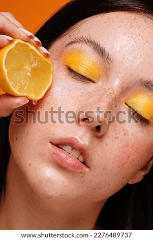 Beauty woman squeezing juicy lemon fruit on her healthy skin with natural freckles . Concept of a clean skin care, cosmetology.
